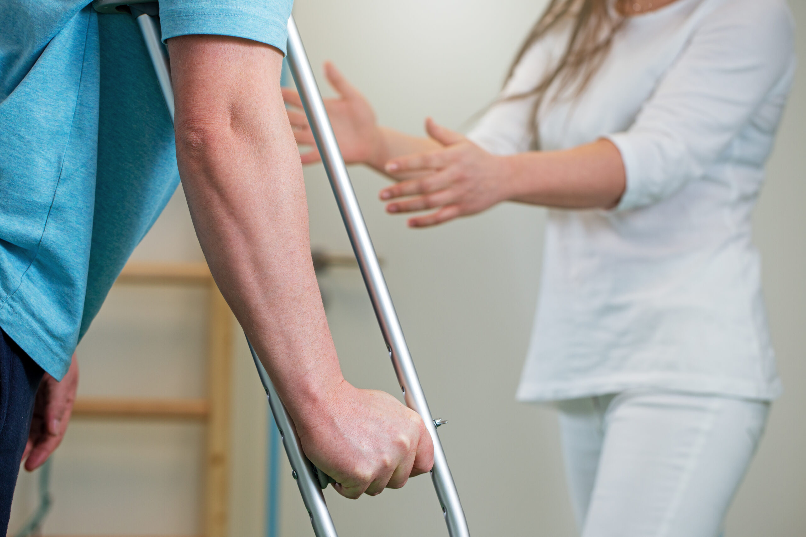 Close Up Of Man Holding Crutch During Rehabilitation With Woman Physiotherapist